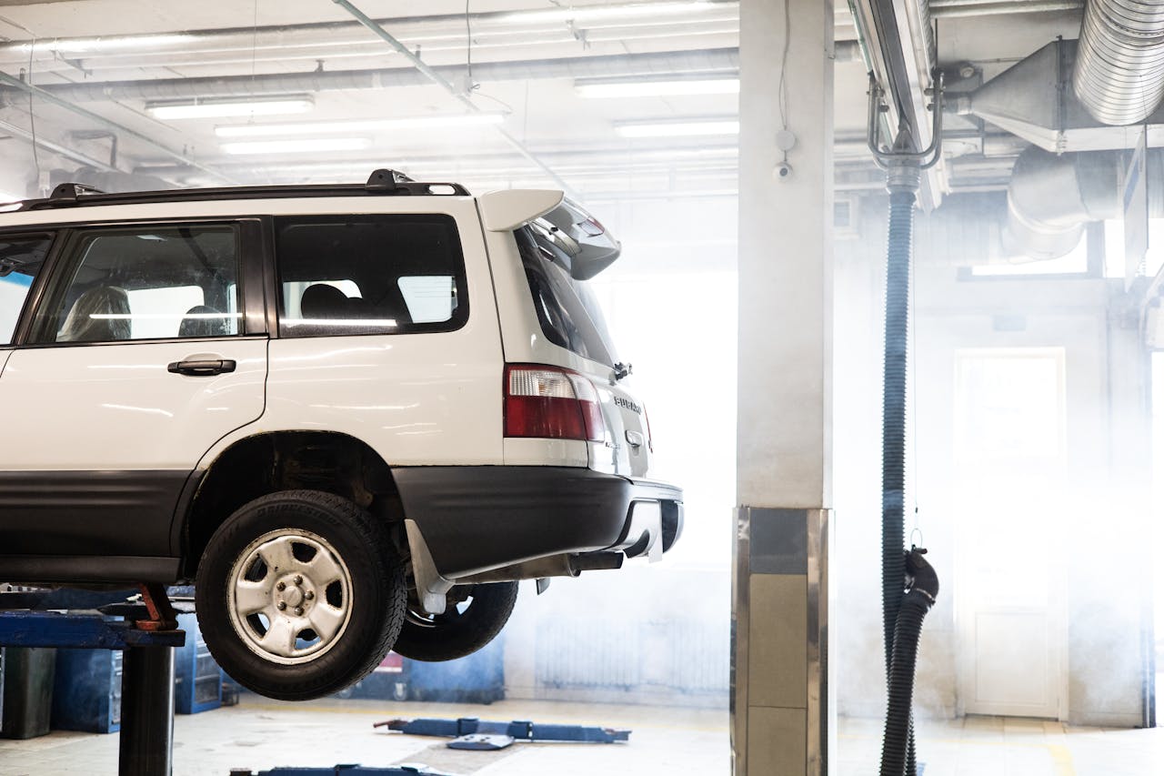 A white SUV is elevated on a lift inside an auto repair shop for maintenance.